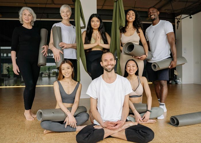 A diverse group of people smiling and preparing for a yoga class.